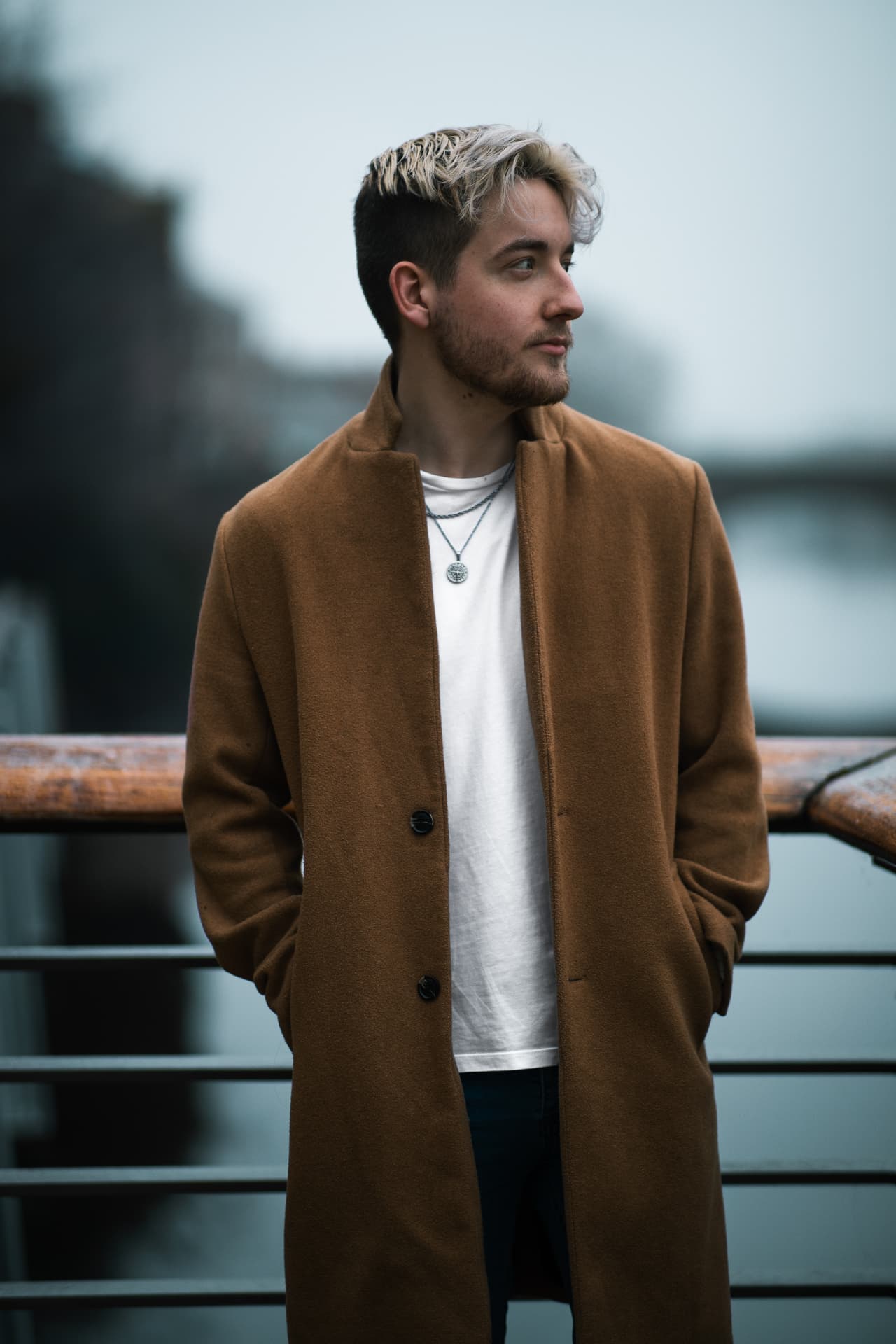 Menswear model in a camel overcoat on a bridge